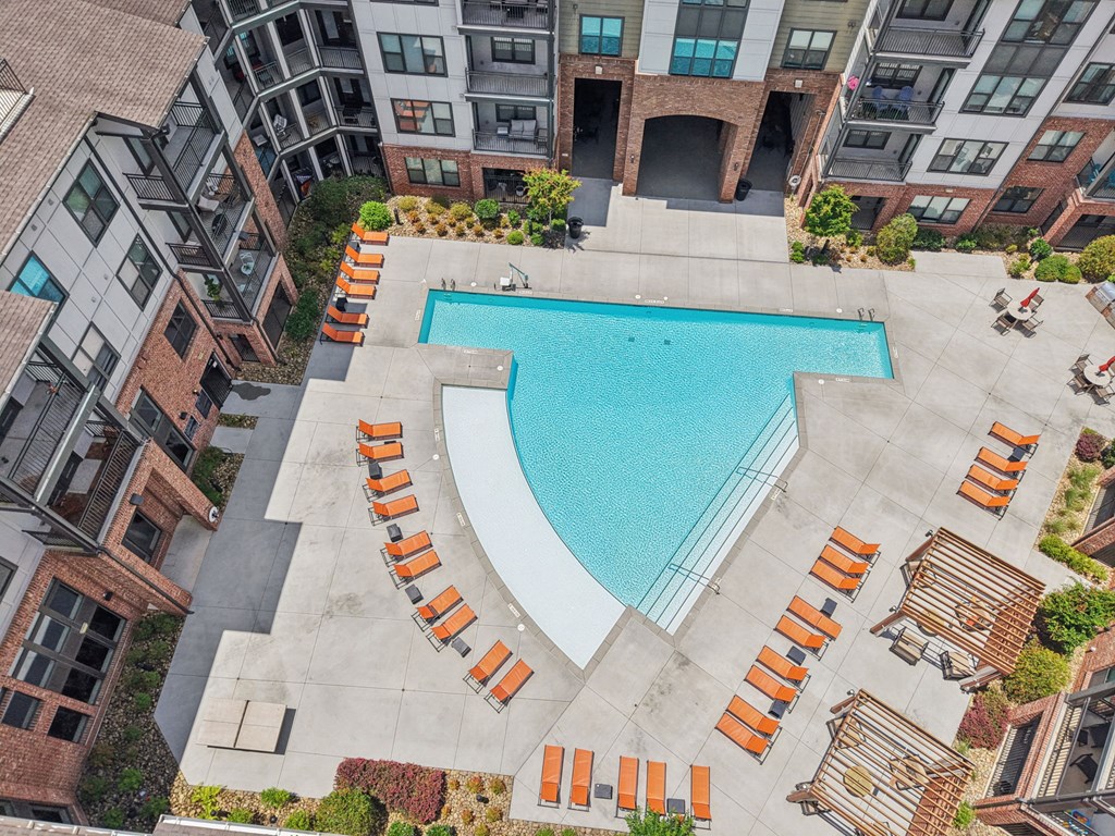 A swimming pool surrounded by orange lounge chairs in a courtyard.